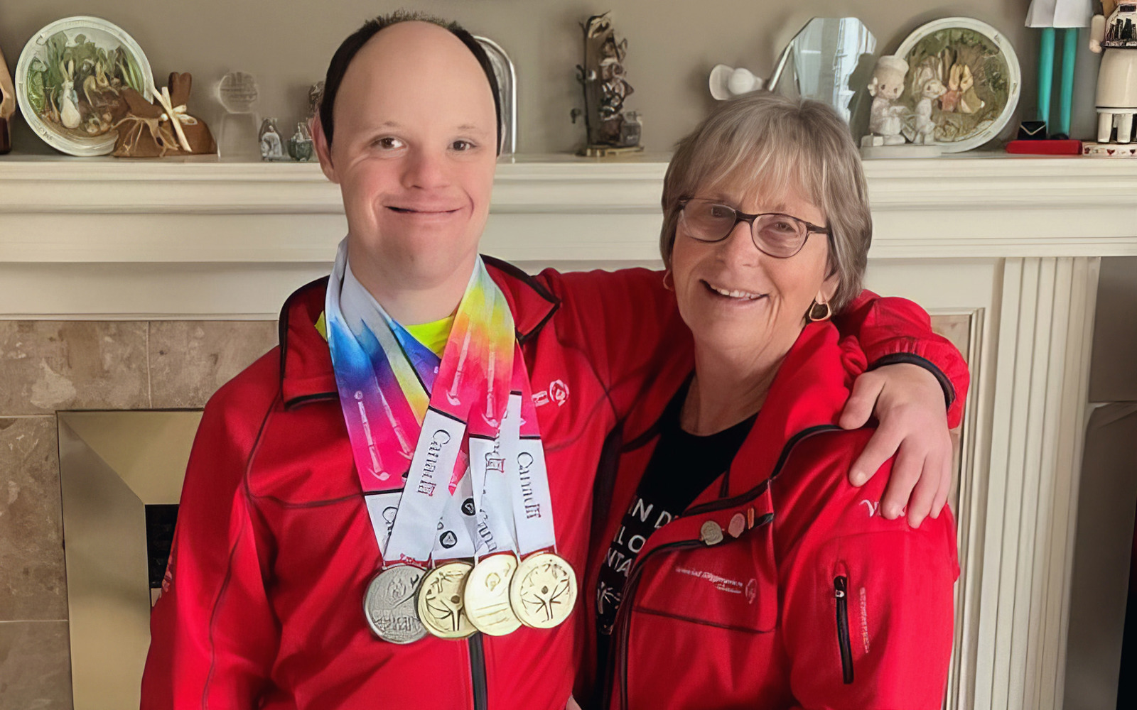 Man in a Special Olympics Team Canada jacket with medals around his neck. He has his arm around a woman, also in a Special Olympics Team Canada jacket. Both are smiling at the camera. 